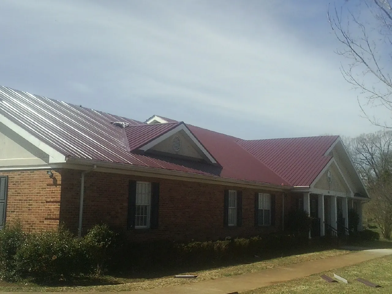 Red metal roof with gabled entries on a long brick building, from a Hail Damage Roof Repair job in Pearl River