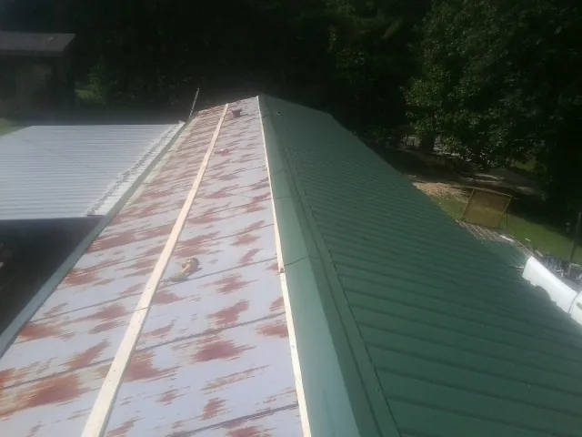 Old rusted panels beside newly installed green metal roofing — Wind Damage Roof Repair by Roofing Brothers in Pearl River