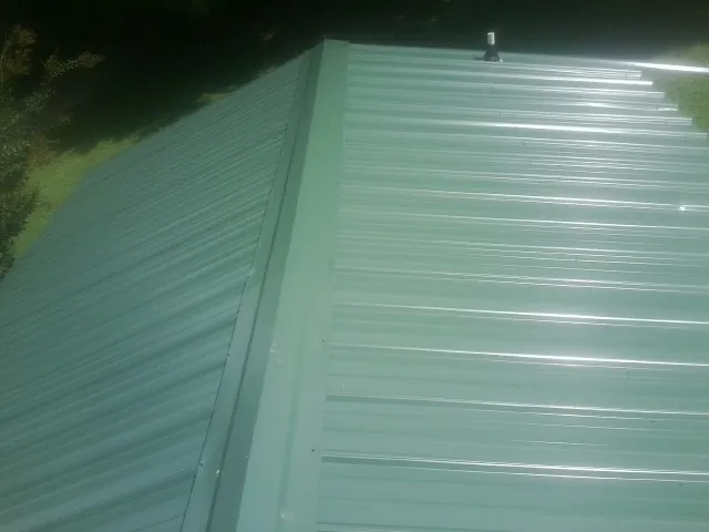 New green metal panels meeting at the ridge of a roof — Flat Roof Repair work by our crew in Pearl River